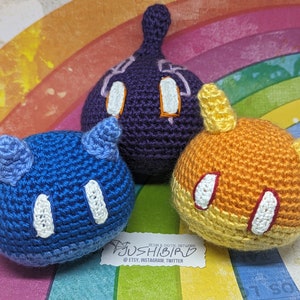 Puede incluir: Tres personajes de peluche tejidos a crochet en forma de fantasma, un personaje azul y un personaje naranja. Los peluches están sentados sobre un fondo de arcoíris. Los peluches tienen ojos blancos y una boca roja. El fondo tiene el texto "#JUSHIBIRD RESIN & DIGITAL ARTWORK @ETSY, INSTAGRAM, TWITTER"