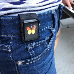 May include: A black silicone protective case holding a smartwatch attached to the waistband of dark blue denim jeans. The watch face displays a yellow and orange butterfly graphic, the time 5:38, and the number 13 in a digital font format.