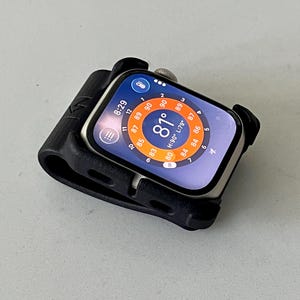 May include: A silver smartwatch encased in a black protective silicone bumper frame. The watch face displays a digital interface with a circular temperature gauge showing 81 degrees, a time of 8:29, and various weather-related data points.