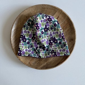 Peut inclure: Un bonnet blanc à imprimé floral avec des fleurs violettes, roses et vertes. Le bonnet a une bordure marron foncé.