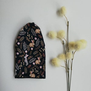 May include: A black beanie with a repeating pattern of brown rabbits and leaves on a dark background.