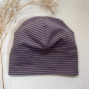 Puede incluir: Un gorro de rayas azul marino y melocotón. El gorro está hecho de una tela suave y presenta rayas horizontales. El gorro está diseñado para ser usado en la cabeza y es adecuado para diversas ocasiones.