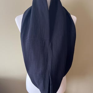 Peut inclure: Une &eacute;charpe noire en forme d'infini en tissu doux et textur&eacute;. L'&eacute;charpe est drap&eacute; sur un mannequin blanc.