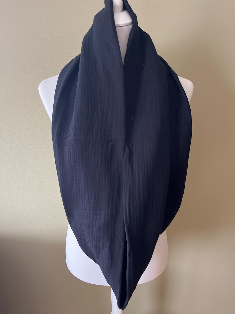 Peut inclure: Une &eacute;charpe noire en forme d'infini en tissu doux et textur&eacute;. L'&eacute;charpe est drap&eacute; sur un mannequin blanc.