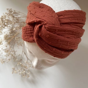 Puede incluir: Una diadema anudada de color óxido con un patrón texturizado de lunares.