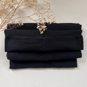 Peut inclure: Un empilement de carr&eacute;s de tissu noir, pli&eacute;s soigneusement. Le tissu a une apparence douce et textur&eacute;e.