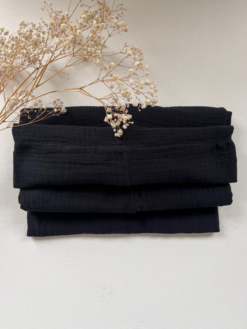 Peut inclure: Un empilement de carr&eacute;s de tissu noir, pli&eacute;s soigneusement. Le tissu a une apparence douce et textur&eacute;e.
