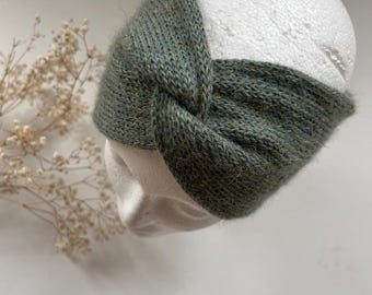 Op de afbeelding: Een groene gebreide hoofdband met een geknoopt ontwerp. De hoofdband is gemaakt van zacht, pluizig garen.