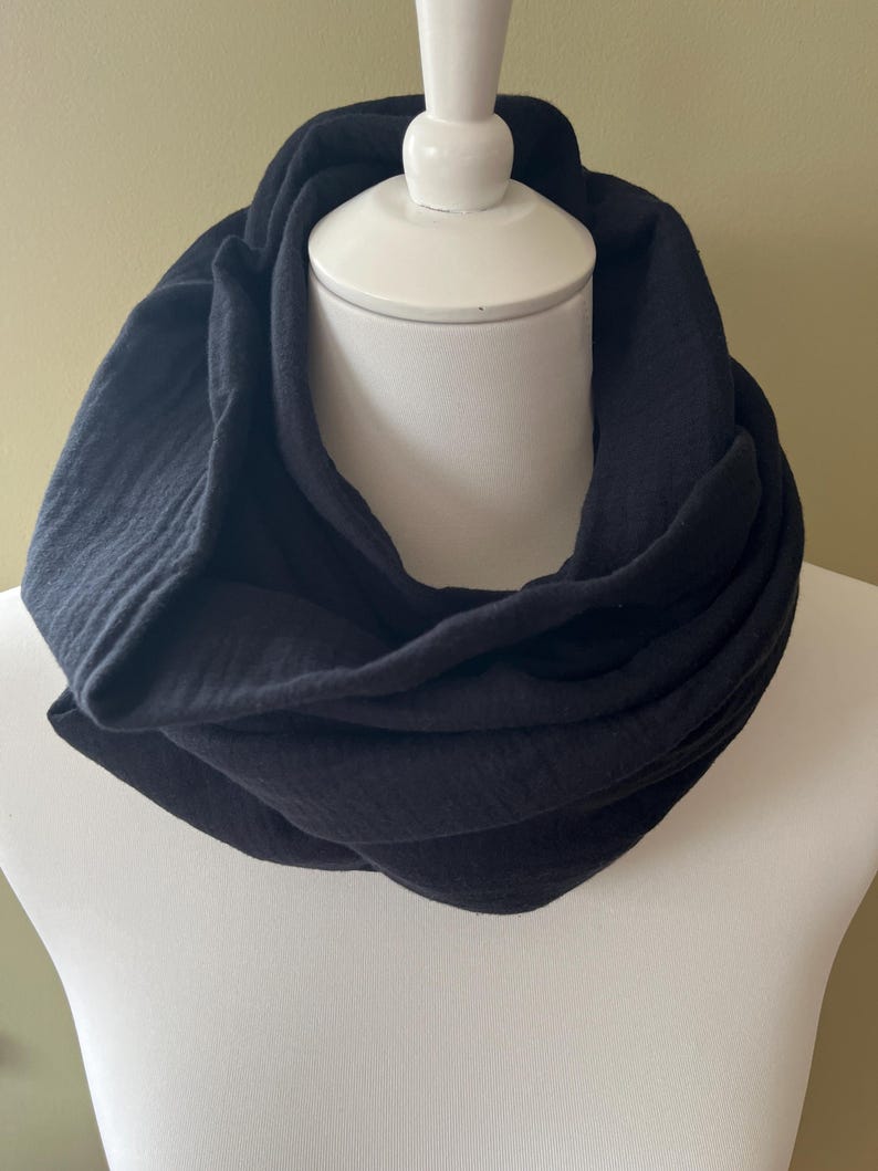 Peut inclure: Une &eacute;charpe noire en tissu doux et textur&eacute;. L'&eacute;charpe est pli&eacute;e et pr&eacute;sent&eacute;e sur un mannequin blanc.