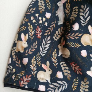 May include: A dark blue fabric with a repeating pattern of white rabbits, brown leaves, and pink flowers.
