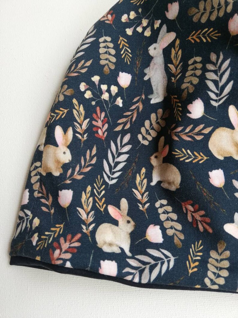 May include: A dark blue fabric with a repeating pattern of white rabbits, brown leaves, and pink flowers.