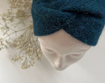 Op de afbeelding: Een tealblauwe gebreide hoofdband met een gedraaid ontwerp. De hoofdband is gemaakt van een zacht, pluche garen.