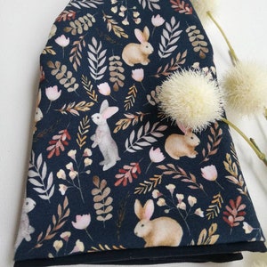 May include: A dark blue fabric with a repeating pattern of brown rabbits, leaves, and flowers. The fabric is folded in half and has a black lining.