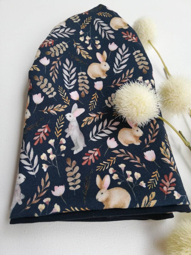 May include: A dark blue fabric with a repeating pattern of brown rabbits, leaves, and flowers. The fabric is folded in half and has a black lining.