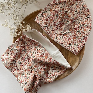 Puede incluir: Un conjunto de dos accesorios a juego con estampado floral. Un gorro y un cuello de color crema con un estampado floral rojo, naranja y verde.