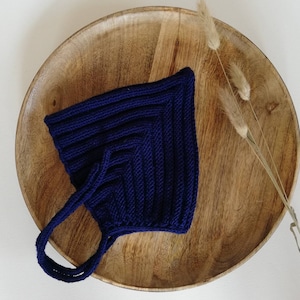 May include: A dark blue knitted tote bag with a square shape and two handles. The bag is sitting on a wooden plate.