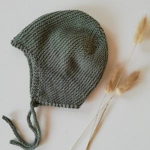 Puede incluir: Un gorro de bebé de punto verde salvia con un lazo en la parte posterior.