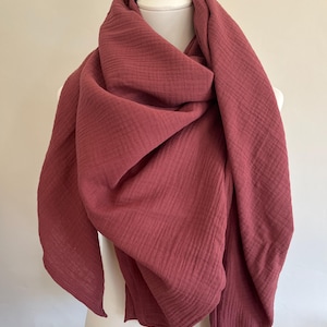 Może przedstawiać: Szary różowy szalik narzucony na biały manekin. Szalik wykonany jest z miękkiej, teksturowanej tkaniny z widocznymi pionowymi żebrami. Szalik jest owinięty wokół szyi i ramion manekina.