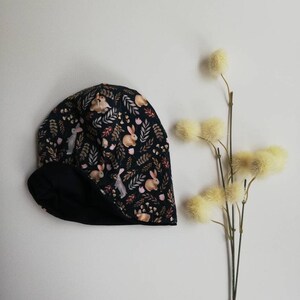 May include: A black and white winter hat with a pattern of bunnies and leaves. The hat has a fleece lining.