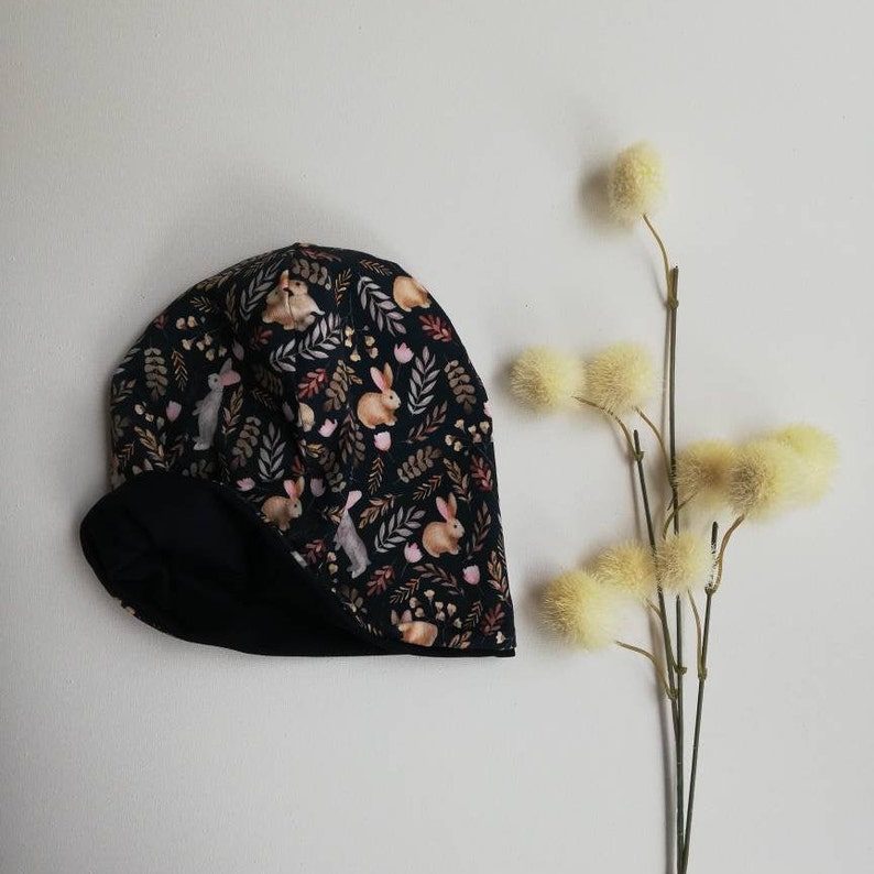 May include: A black and white winter hat with a pattern of bunnies and leaves. The hat has a fleece lining.