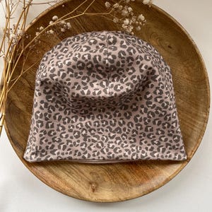 Könnte beinhalten: Eine braune und rosafarbene Mütze mit Leopardenmuster auf einem Holzteller.