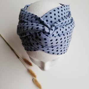 Op de afbeelding: Een lichtblauw hoofdband met een donkerblauw stippenpatroon. Het hoofdband is bovenop het hoofd in een knoop geknoopt.