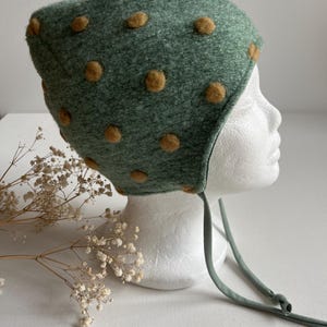 May include: A green felt baby bonnet with brown felt polka dots and a tie string.