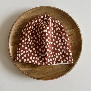 Pode incluir: Um gorro marrom com um padrão de bolinhas brancas. O gorro está em um prato de madeira.