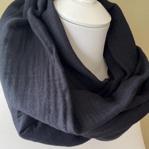 Peut inclure: Une &eacute;charpe noire en forme d'infini en tissu doux et textur&eacute;. L'&eacute;charpe est drap&eacute; sur un mannequin blanc.