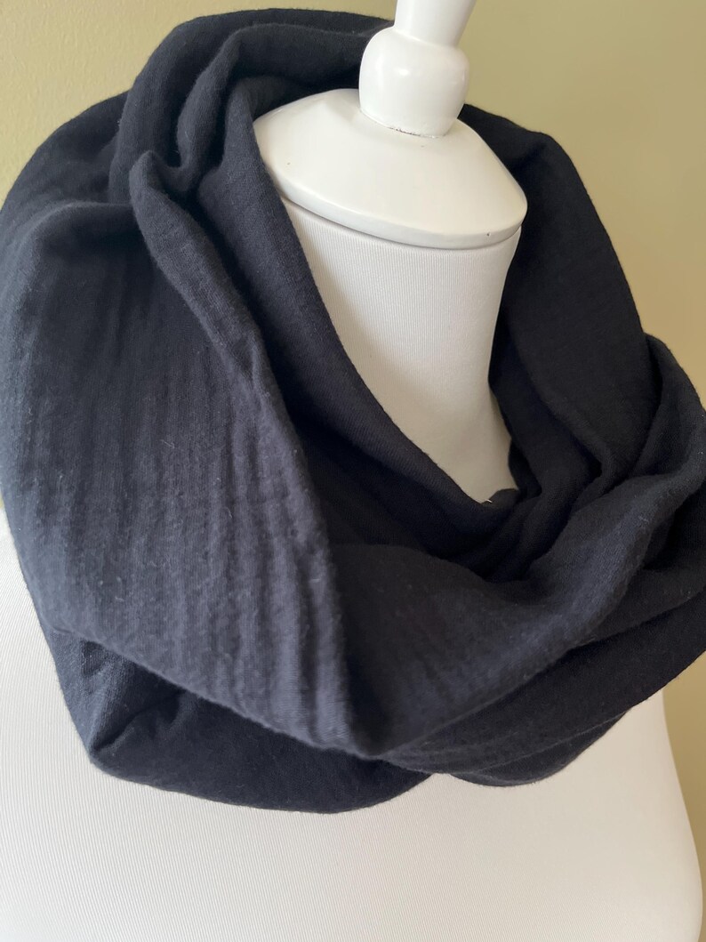 Peut inclure: Une &eacute;charpe noire en forme d'infini en tissu doux et textur&eacute;. L'&eacute;charpe est drap&eacute; sur un mannequin blanc.