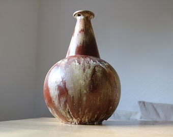 May include: A brown ceramic vase with a rounded body and a narrow neck. The vase has a mottled glaze with brown, white, and beige accents.