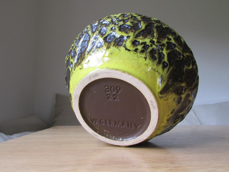 May include: Yellow and brown ceramic vase with a mottled glaze. The bottom of the vase has a brown label with the text "309 22 W GERMANY".