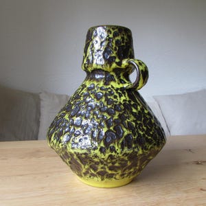 May include: A yellow and brown ceramic vase with a textured surface and a handle. The vase has a unique, abstract design.
