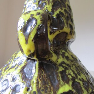 May include: A yellow and brown ceramic vase with a textured surface and a handle. The vase has a mottled glaze with a speckled pattern.
