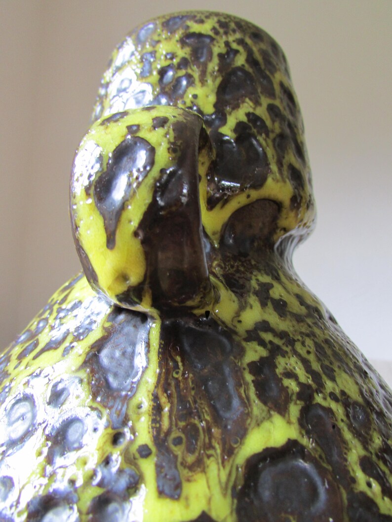 May include: A yellow and brown ceramic vase with a textured surface and a handle. The vase has a mottled glaze with a speckled pattern.