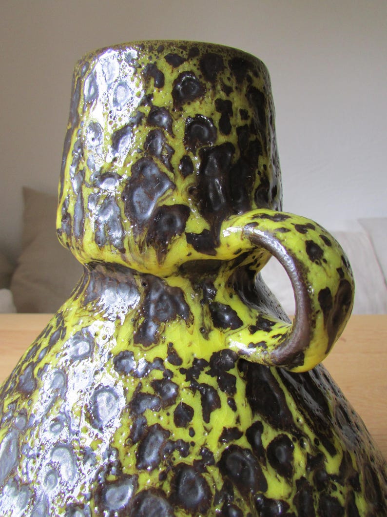 May include: A yellow and brown ceramic vase with a textured surface and a handle. The vase has a unique, abstract design.