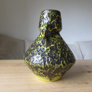 May include: A yellow and brown ceramic vase with a textured, speckled surface. The vase has a wide base and a narrow neck.