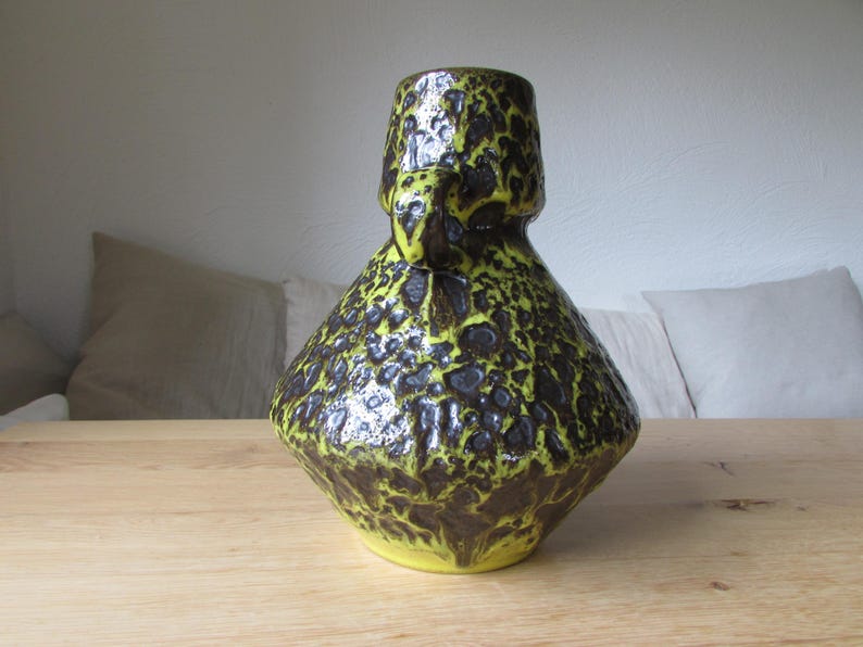 May include: A yellow and brown ceramic vase with a textured, speckled surface. The vase has a wide base and a narrow neck.