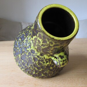 May include: A yellow and brown ceramic vase with a textured surface. The vase has a wide opening and a unique shape.