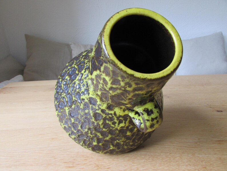 May include: A yellow and brown ceramic vase with a textured surface. The vase has a wide opening and a unique shape.