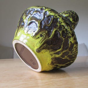 May include: A yellow and brown ceramic vase with a textured surface. The vase has a unique, organic shape and is made in Germany.