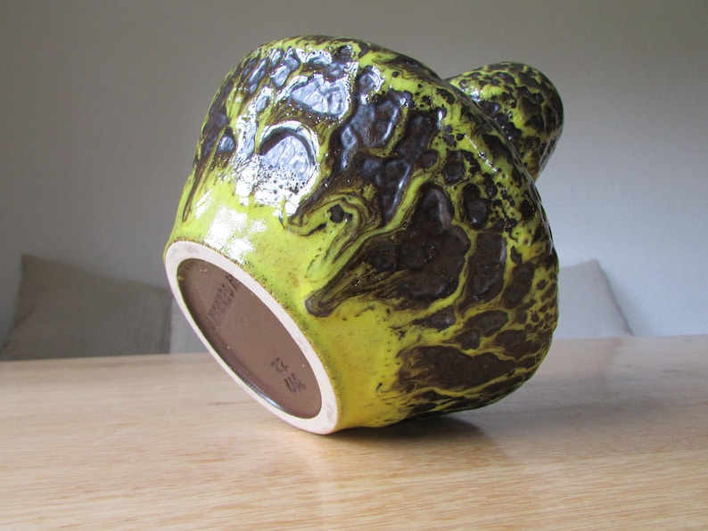 May include: A yellow and brown ceramic vase with a textured surface. The vase has a unique, organic shape and is made in Germany.