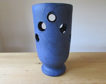 May include: A blue ceramic vase with a textured surface and multiple circular cutouts. The vase has a flared base.
