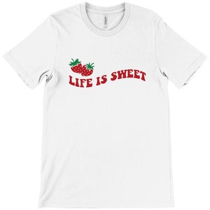 Op de afbeelding: Wit T-shirt met een rode afbeelding van twee aardbeien en de tekst "LIFE IS SWEET" in rood.