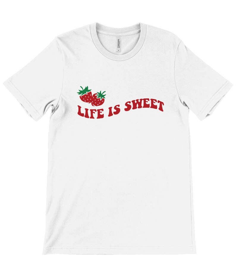 Op de afbeelding: Wit T-shirt met een rode afbeelding van twee aardbeien en de tekst "LIFE IS SWEET" in rood.
