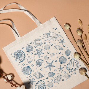 May include: A white canvas tote bag with blue illustrations of seashells, starfish, and bubbles. The bag has two handles.
