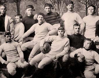 May include: A black and white photograph of a group of men in athletic uniforms, likely a football team. They are standing in a group, some holding a football, and all are wearing hats.