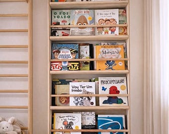 May include: A wooden bookshelf filled with colorful children's books. The bookshelf is mounted on a white wall and has several shelves holding various book titles. A wooden ladder is visible on the left side of the image.