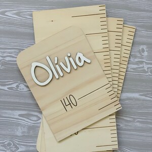 Peut inclure: Un tableau de croissance en bois avec une plaque nominative indiquant "Olivia" et une ligne de mesure marqu&eacute;e "140".