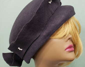 May include: A black felt hat with a wide brim and a decorative bow. The hat has three pearl-like embellishments on the front.